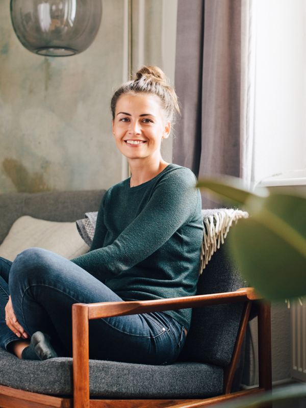 Eine junge Frau sitzt auch eine grünen Sofa und Blickt in die Kamera.